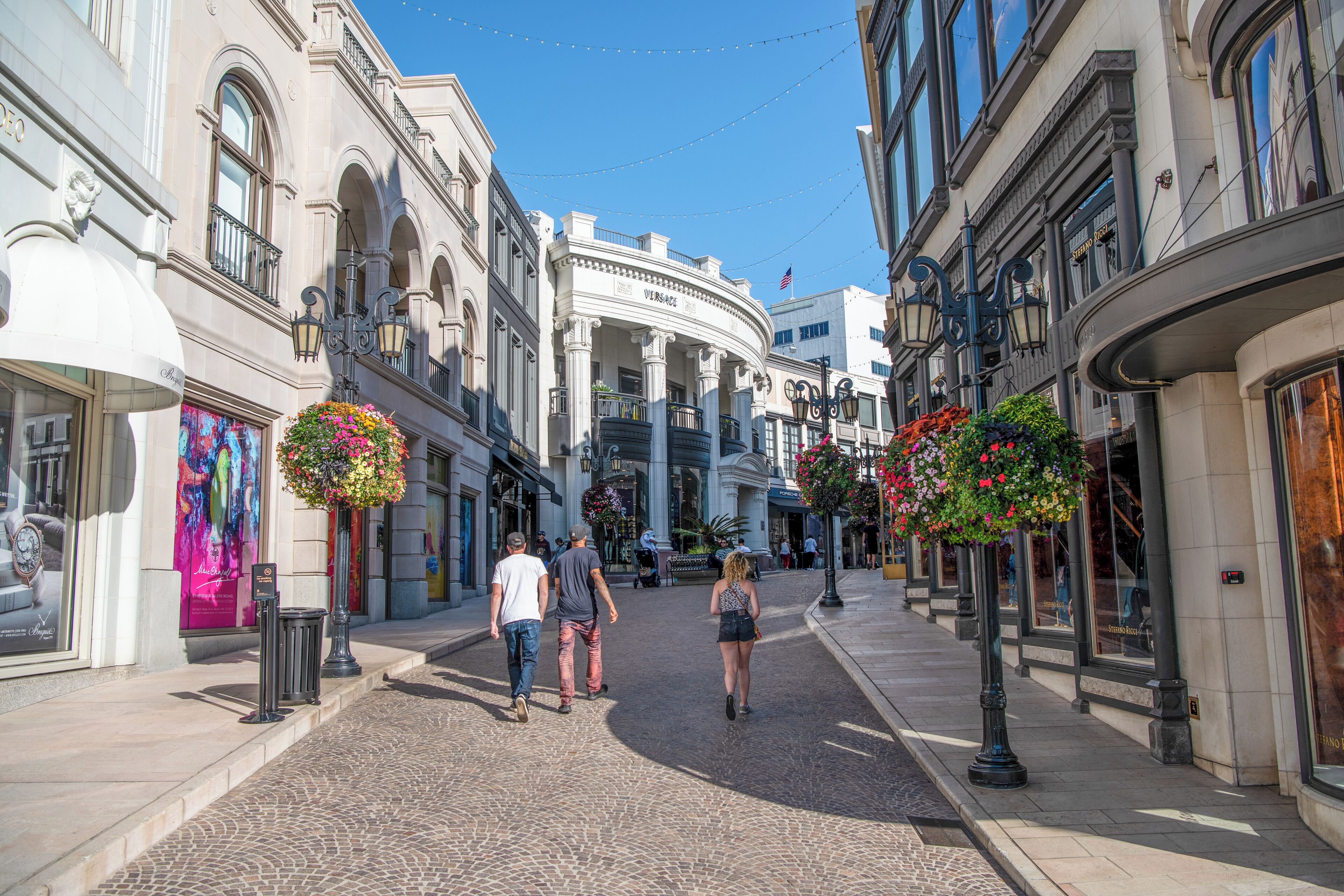A cobblestone street lined with historic buildings, a fountain, and hanging flower baskets.