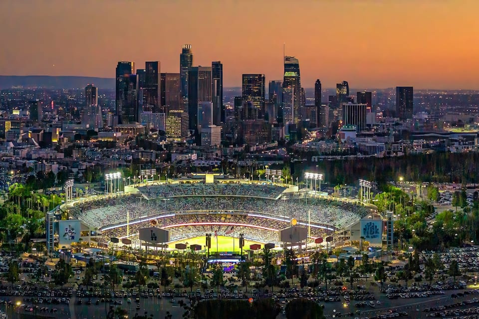 Un horizonte urbano al atardecer con un estadio grande rodeado de estacionamientos y árboles.