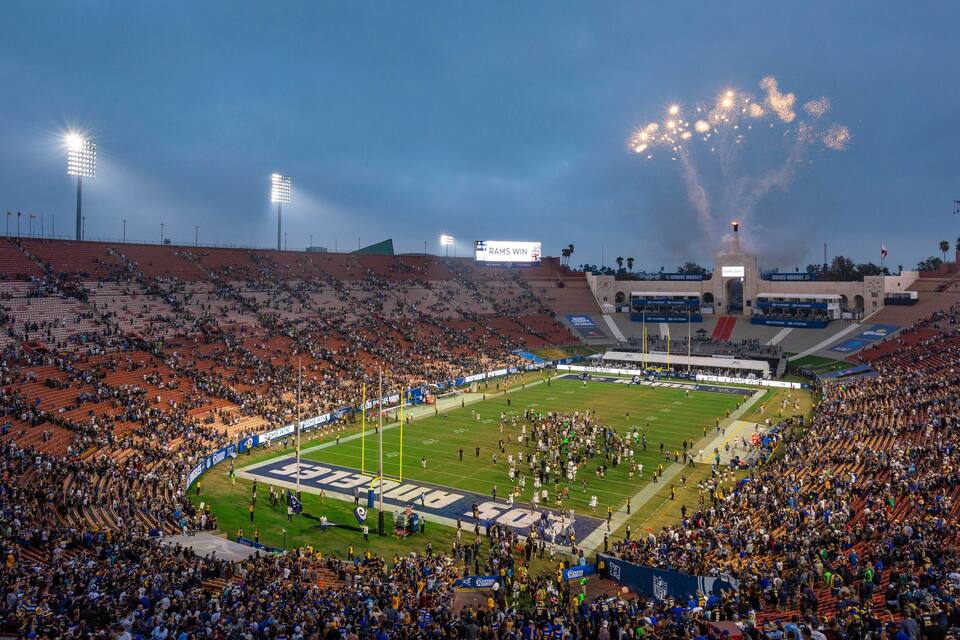 A football stadium with a large crowd, a football field, and stadium lights.