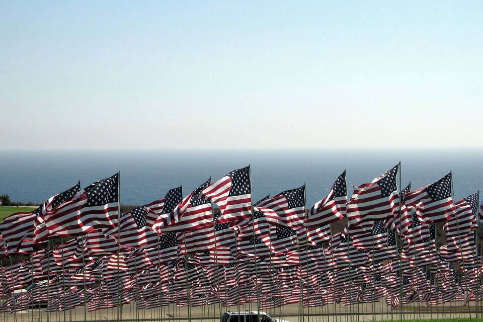 De nombreux drapeaux américains flottent au vent, avec l’océan en toile de fond.