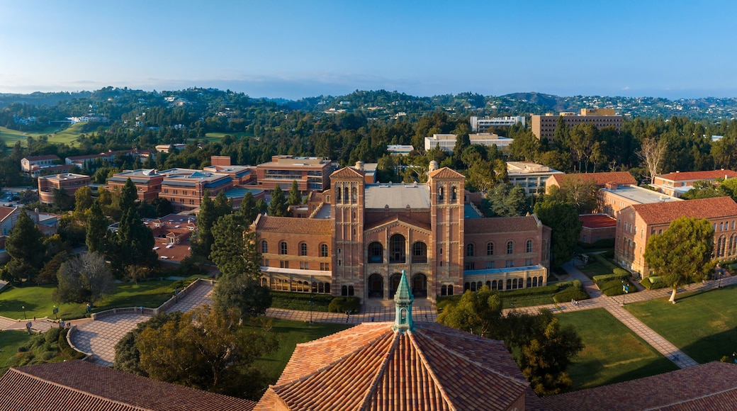 Aerial view of UCLA campus featuring classical architecture, red-brick buildings, green spaces, and a distinctive domed structure under a clear blue sky.