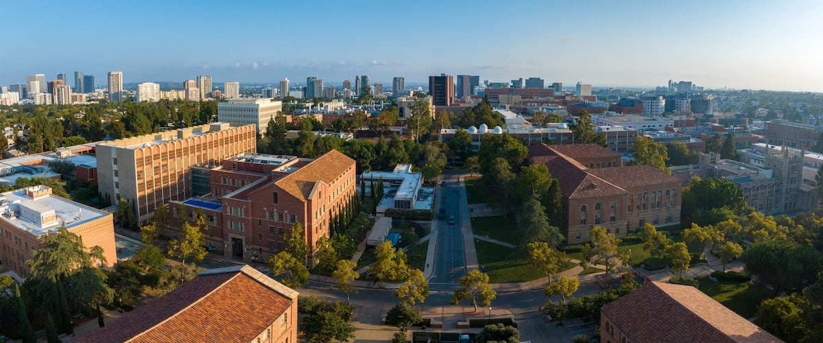 Panoramic early morning view of a serene university campus, blending historic brick buildings with modern high-rises, surrounded by lush greenery and distant ocean vistas.