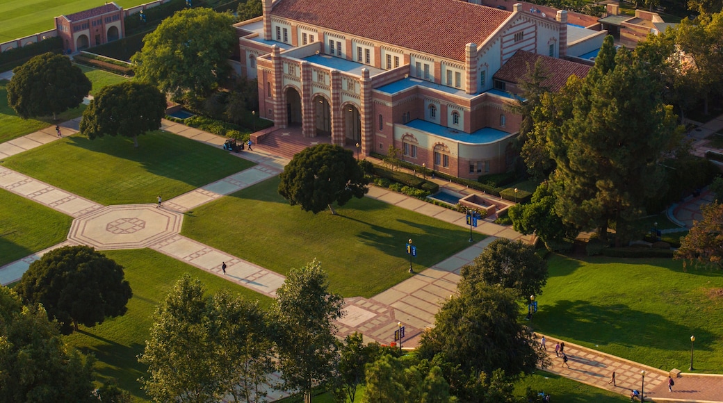 Aerial view of a grand university campus with red-bricked buildings, green lawns, and classical architecture, featuring a sports field, pond, and serene outdoor seating areas.