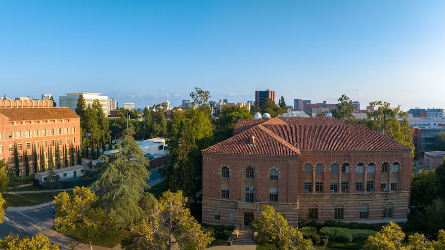 Aerial view of the University of Southern California campus, showcasing historic red-brick buildings, lush greenery, and a scenic city backdrop under a clear blue sky.