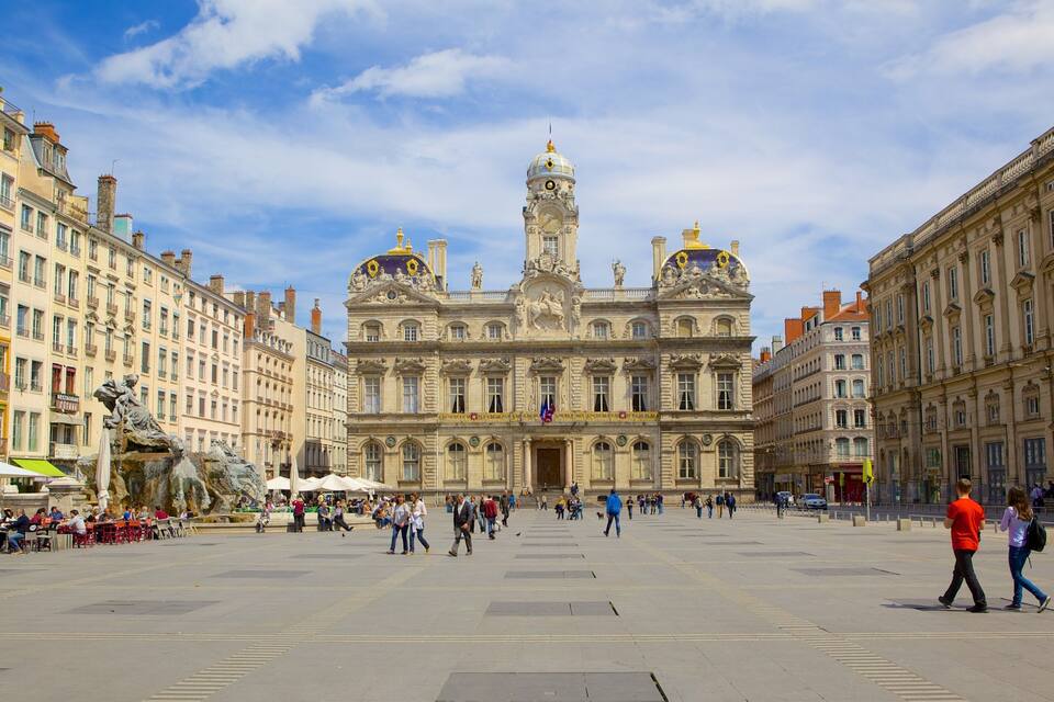 A grand historic building with ornate architecture, a large open square, and surrounding cafes.