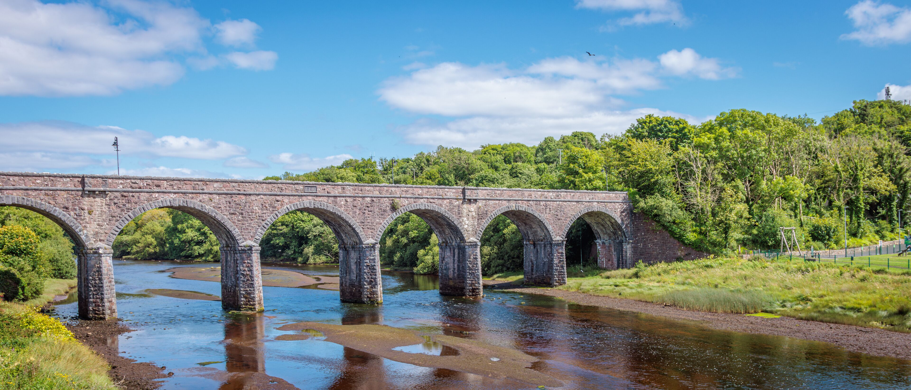 A stone bridge over a river with greenery on both sides.