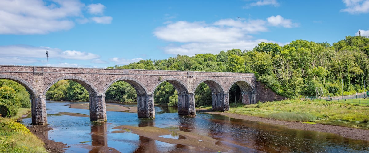 A stone bridge over a river with greenery on both sides.