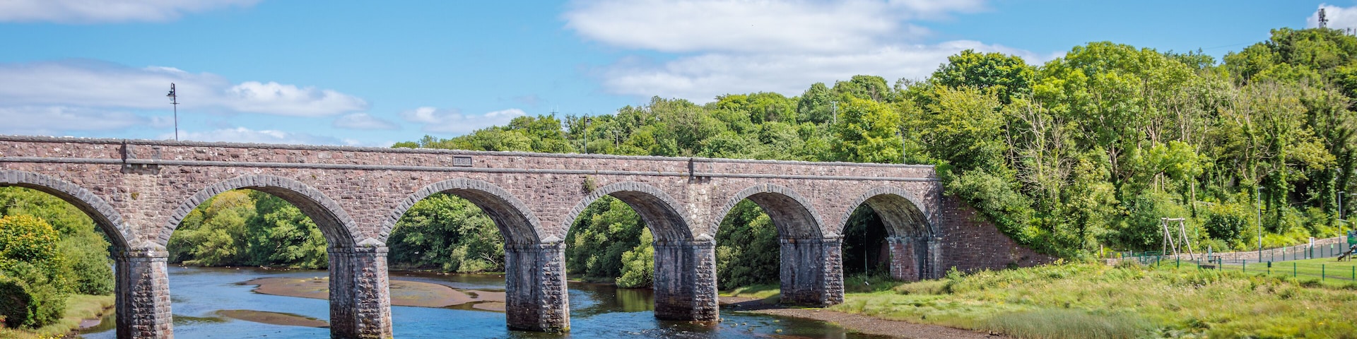 A stone bridge over a river with greenery on both sides.