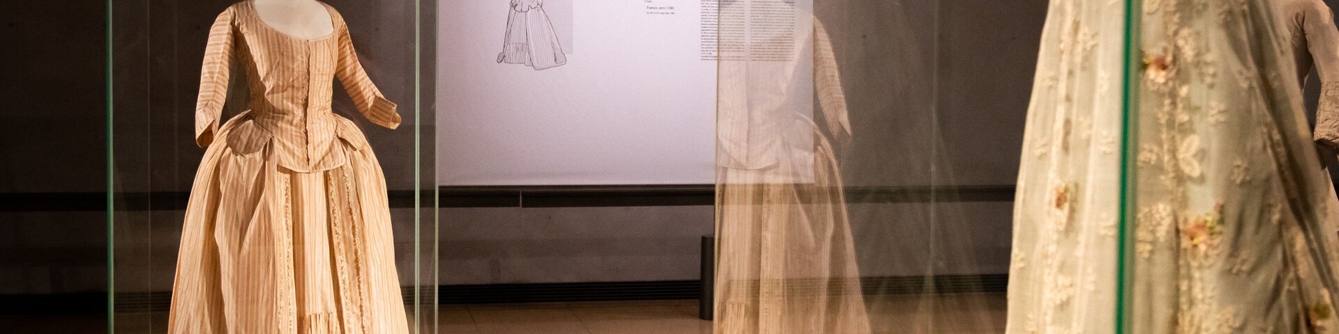 Una vitrina de museo con un maniquí vestido a rayas y otro con un vestido floral.