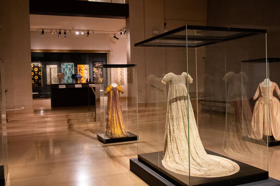 A museum interior with glass display cases containing historical dresses.
