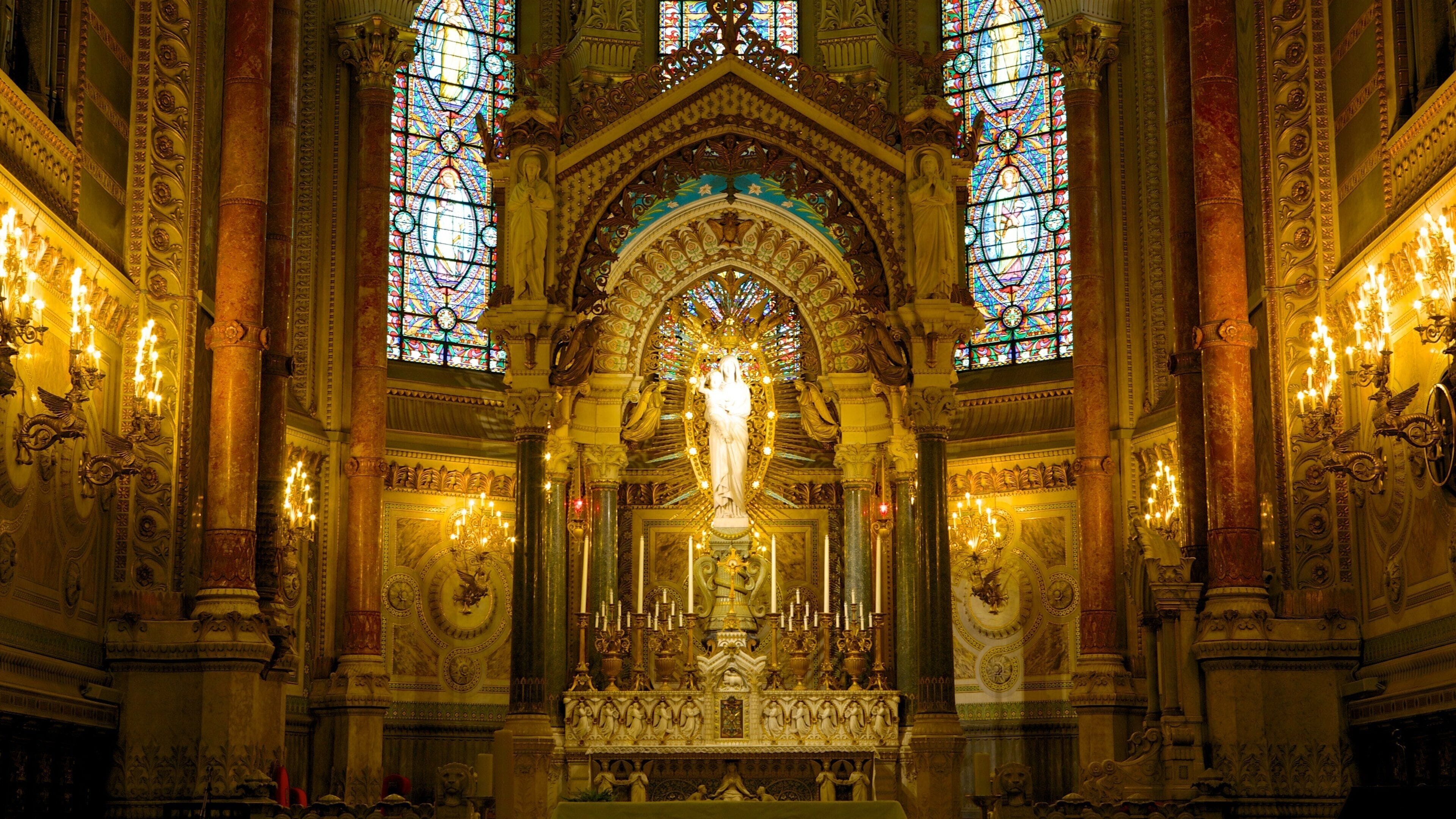 Een versierd kerkinterieur met glas-in-loodramen, een centraal standbeeld en ingewikkelde architectonische details.