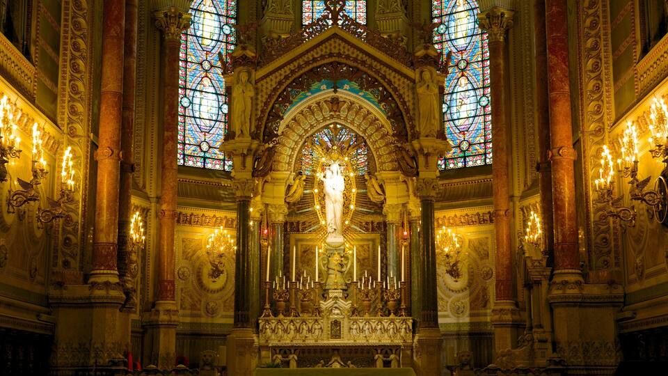 Een versierd kerkinterieur met glas-in-loodramen, een centraal standbeeld en ingewikkelde architectonische details.