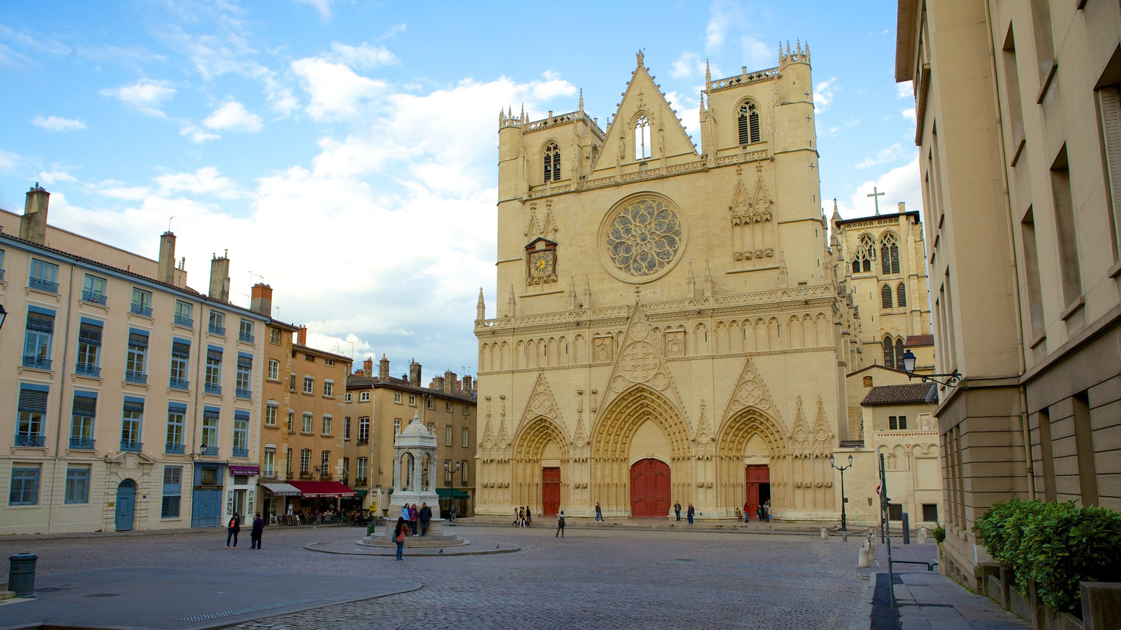 Una catedral histórica con arquitectura gótica detallada, un amplio ventanal circular con vidrieras policromadas y una plaza empedrada al frente.