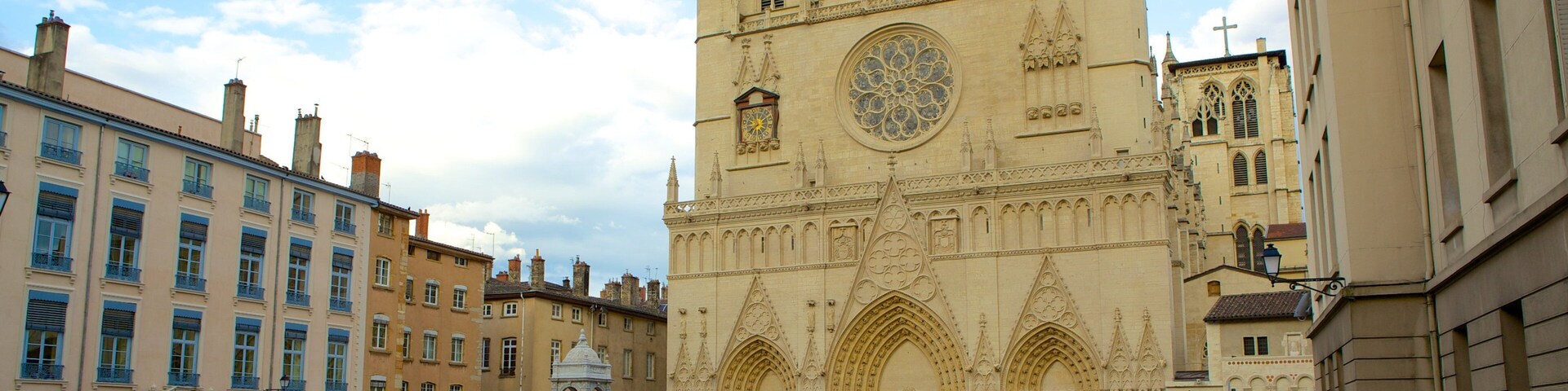 Una catedral histórica con arquitectura gótica detallada, un amplio ventanal circular con vidrieras policromadas y una plaza empedrada al frente.