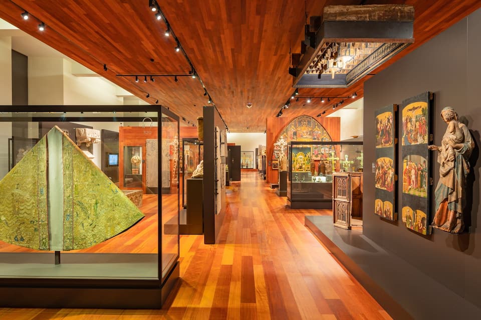 An art gallery with wooden floors, wooden ceiling, and various artworks on display.