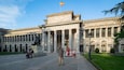 A grand building with classical architecture, featuring columns, statues, and a flag.
