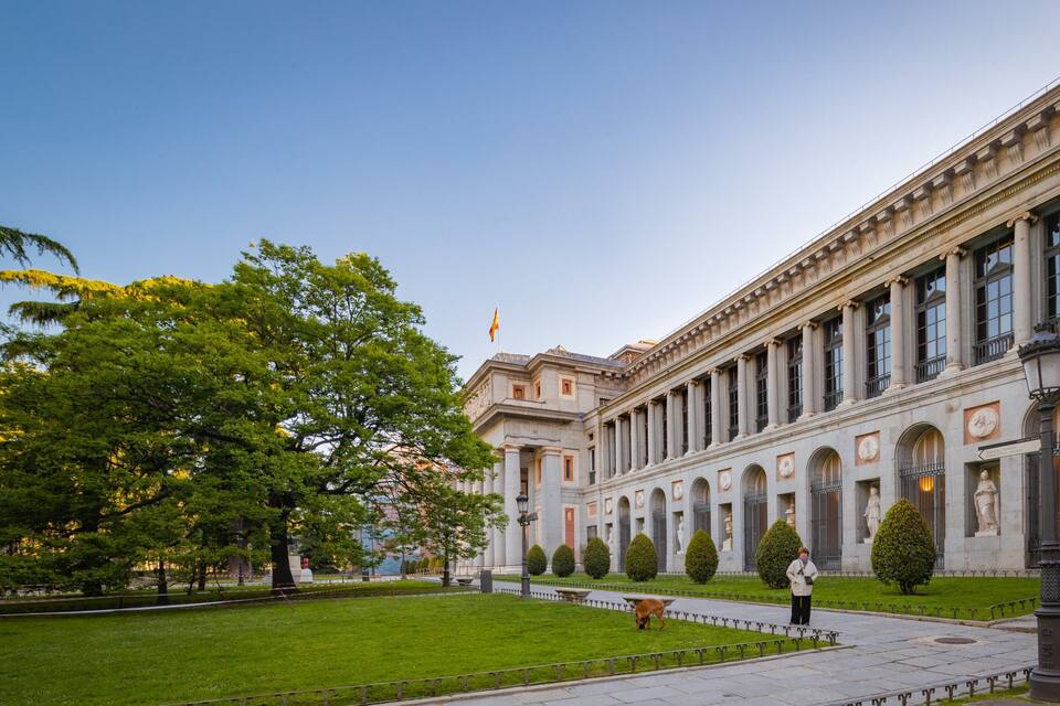 Ein historisches Gebäude mit klassischer Architektur, einem gepflegten Rasen und einer Statue.