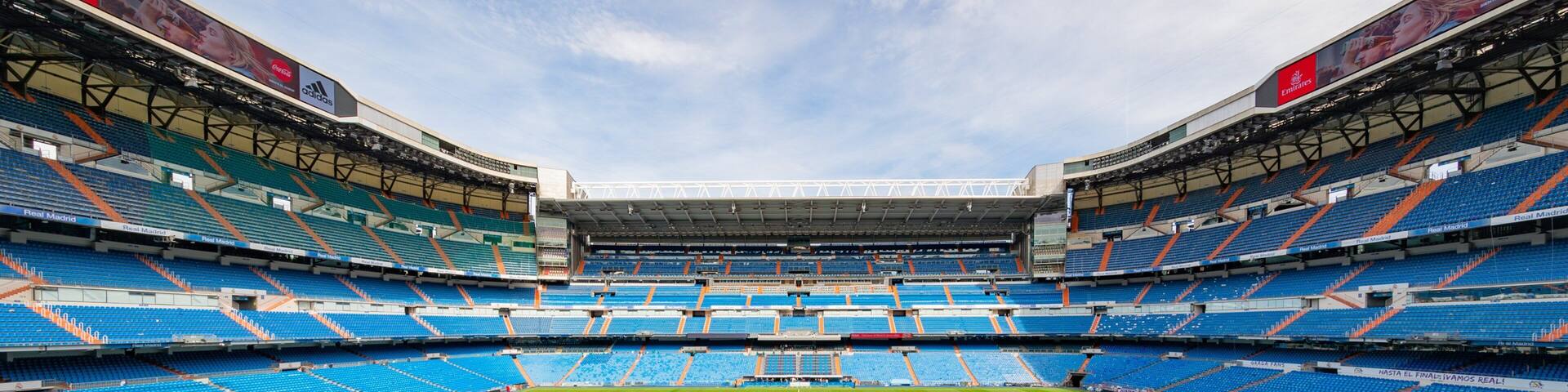 A large, empty stadium with blue seats and a green field.