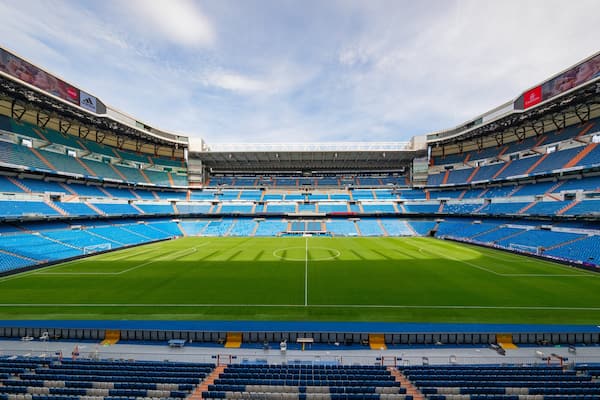 A large, empty stadium with blue seats and a green field.