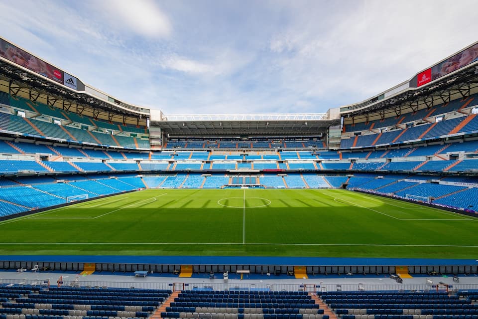 A large, empty stadium with blue seats and a green field.