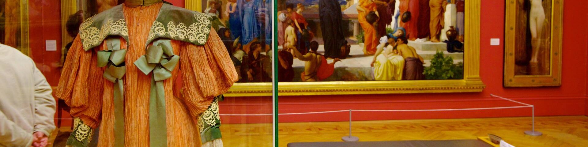 Una exhibición de museo con un maniquí vestido con traje tradicional y dos grandes cuadros en la pared.