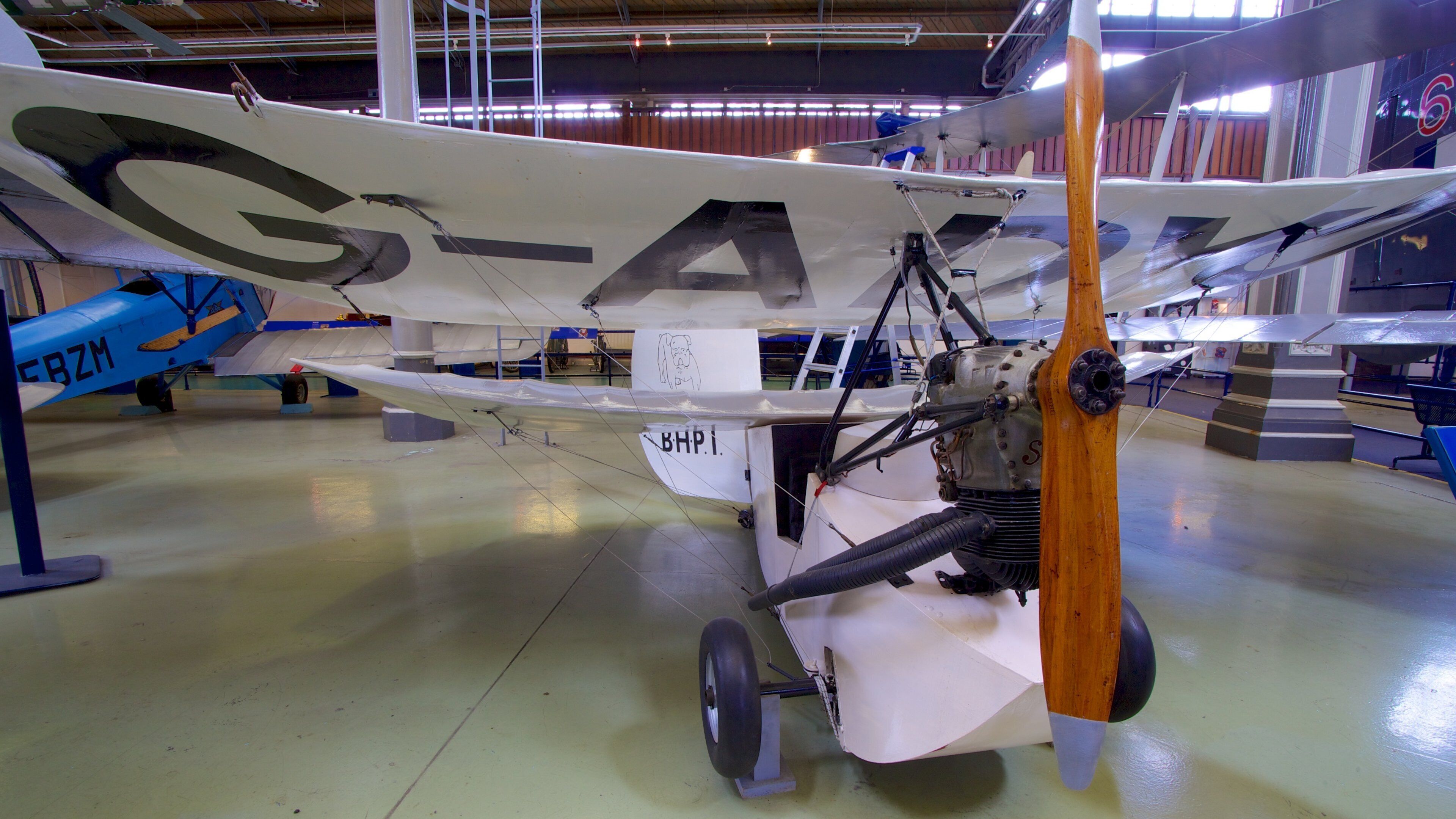 Un biplano antiguo con el número de registro "G-A" y "BHP1" en un hangar de museo.