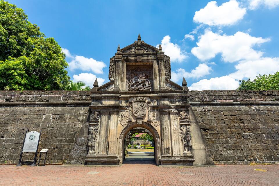 Un antiguo portón de piedra con elaboradas esculturas y un arco central.
