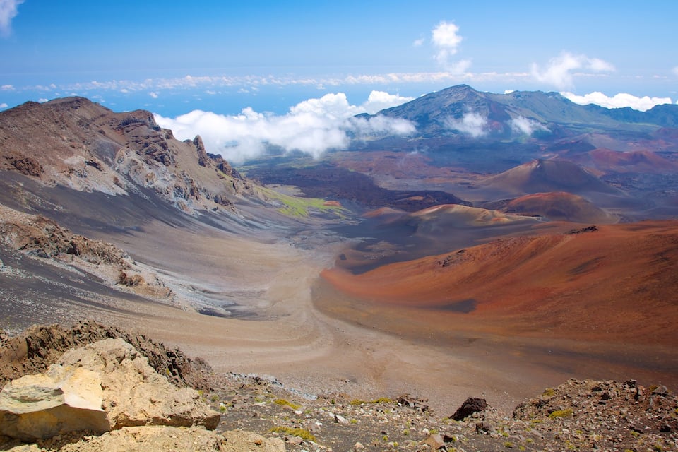 A rugged mountain landscape with a valley and distant peaks under a clear sky.