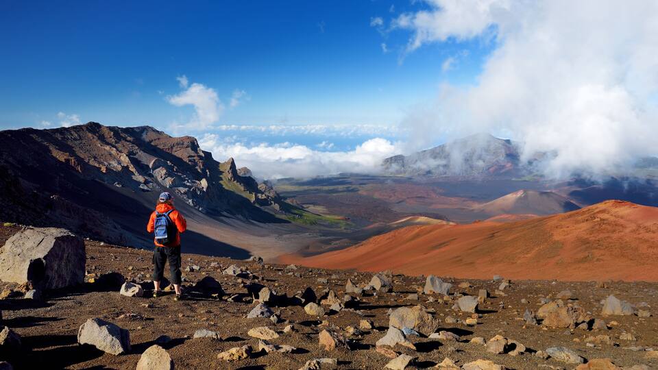 A hiker on a rocky mountain path with a clear sky and distant clouds.