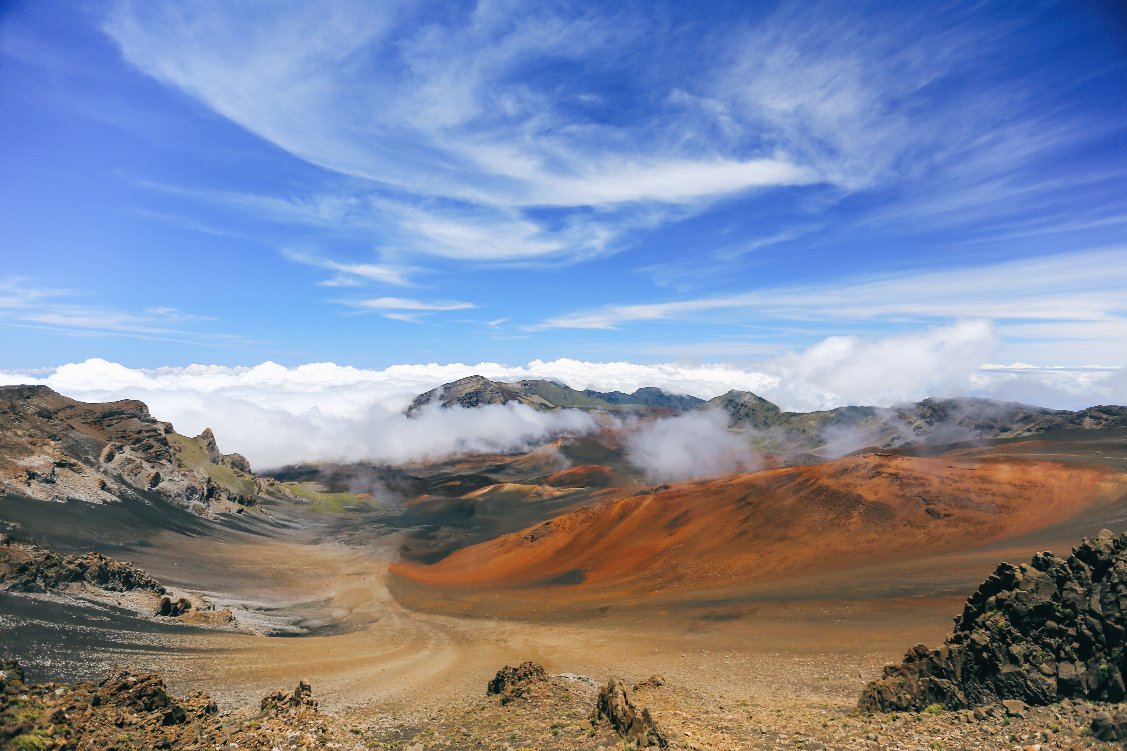 A volcanic landscape with orange and brown hues, a clear sky, and distant mountains.