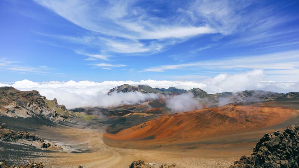 A volcanic landscape with orange and brown hues, a clear sky, and distant mountains.