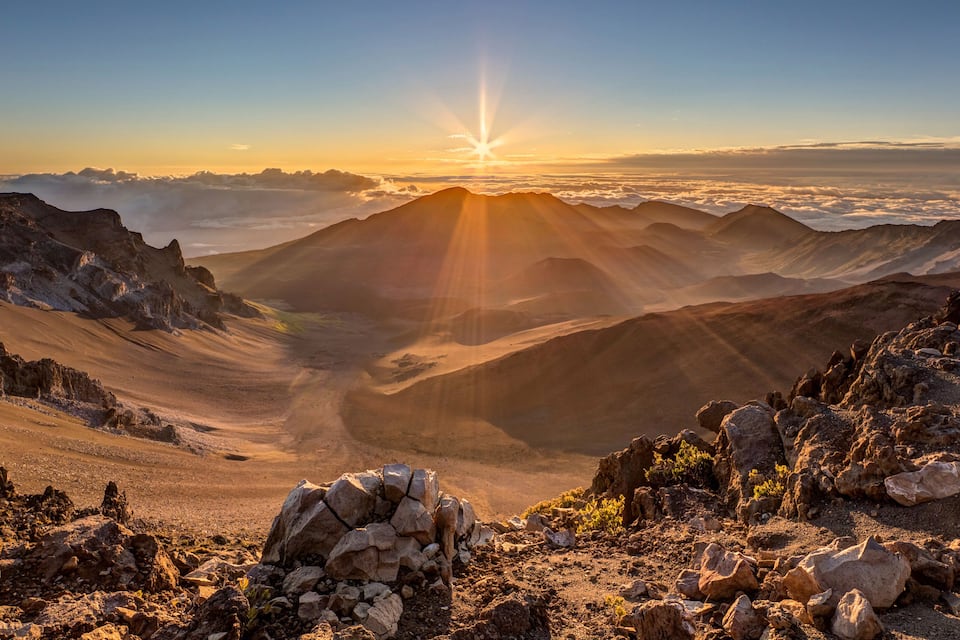 Paesaggio montuoso con una valle illuminata dal sole e terreno roccioso.