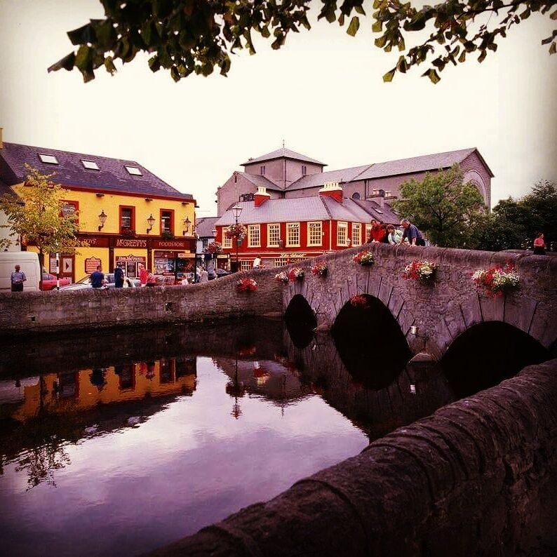 A stone bridge over a canal with buildings on either side, including a yellow building with 'MIGGERS' and a red building with 'FISHERMAN'.