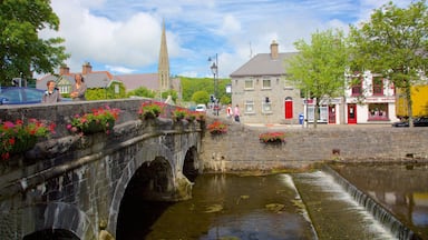 A stone bridge over a canal with flower boxes, a church spire, and a red building with a sign.