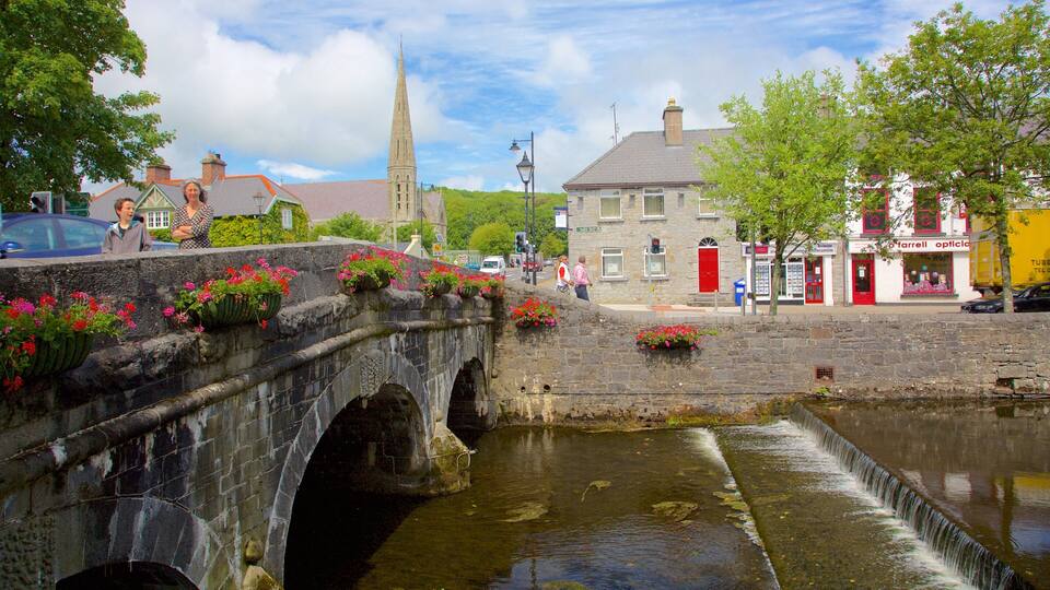 A stone bridge over a canal with flower boxes, a church spire, and a red building with a sign.