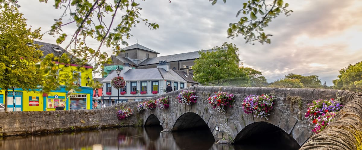 Un puente de piedra con jardineras de flores, un río tranquilo y edificios coloridos.