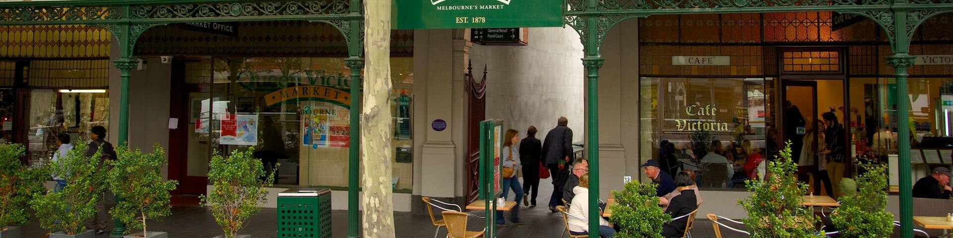 The Queen Victoria Market with a green archway, outdoor seating, and people walking by.