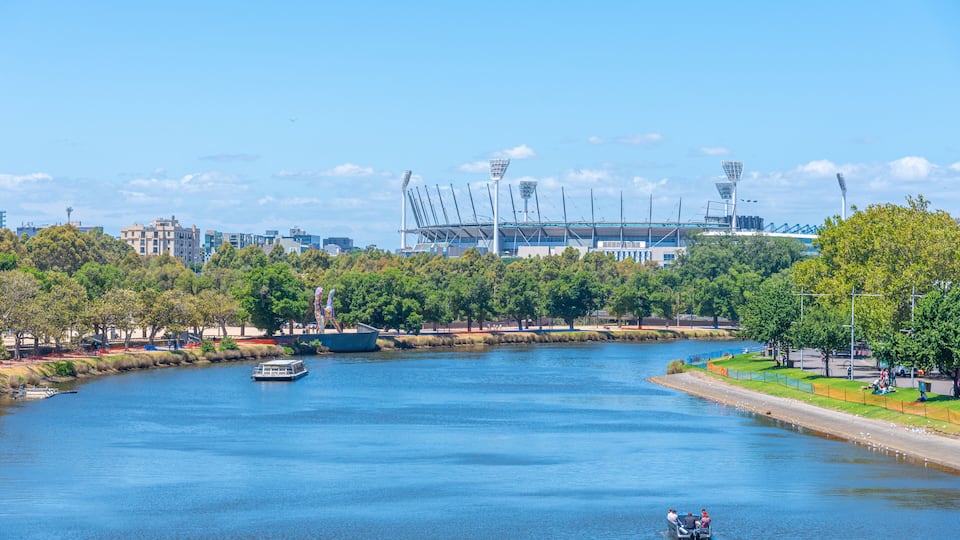 A river with boats, a stadium, and trees.
