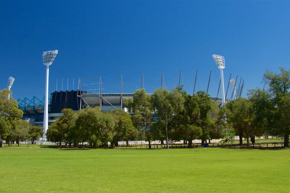 A stadium with floodlights, green grass, and trees.