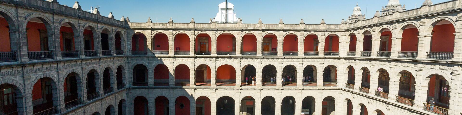 A historic courtyard with a central fountain, surrounded by arches and a flagpole.