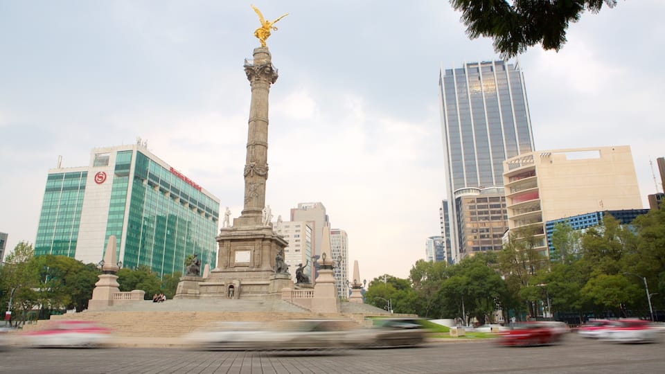 A monument with statues, surrounded by modern buildings and trees.