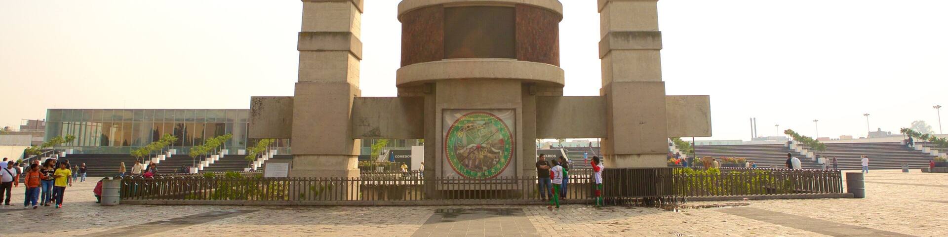 A large clock tower with a sundial in the center, surrounded by a fence and steps leading up to it.