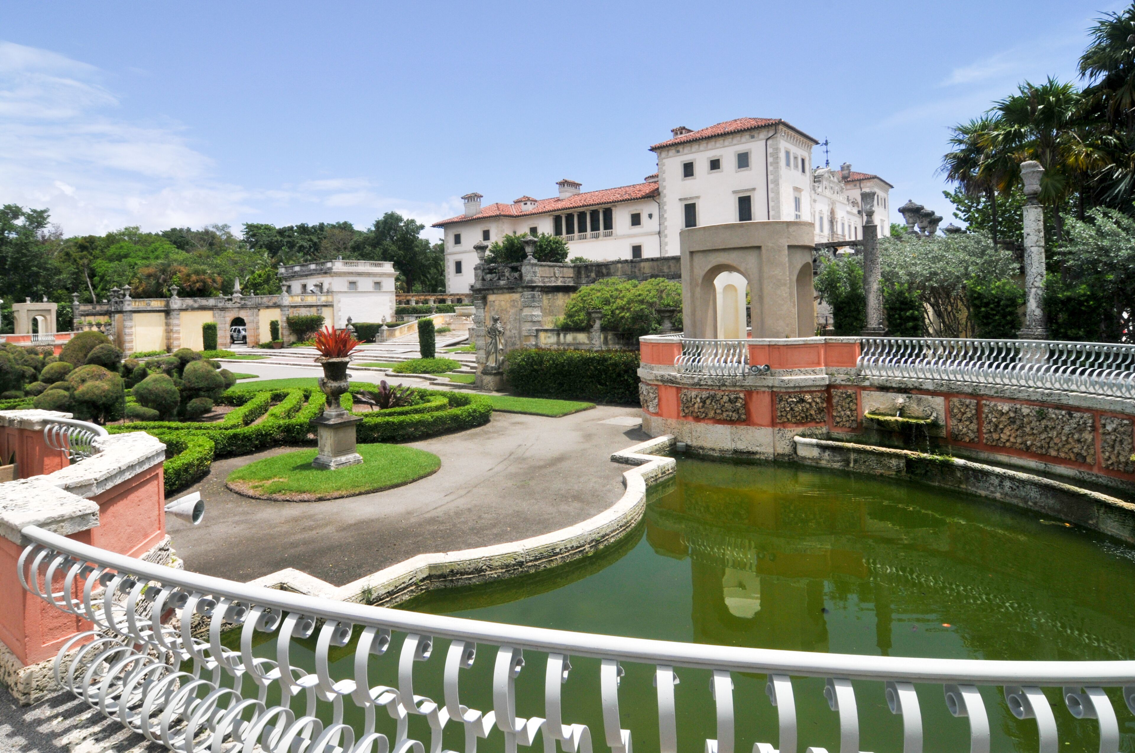 A formal garden with a central pond, manicured hedges, and classical architecture.