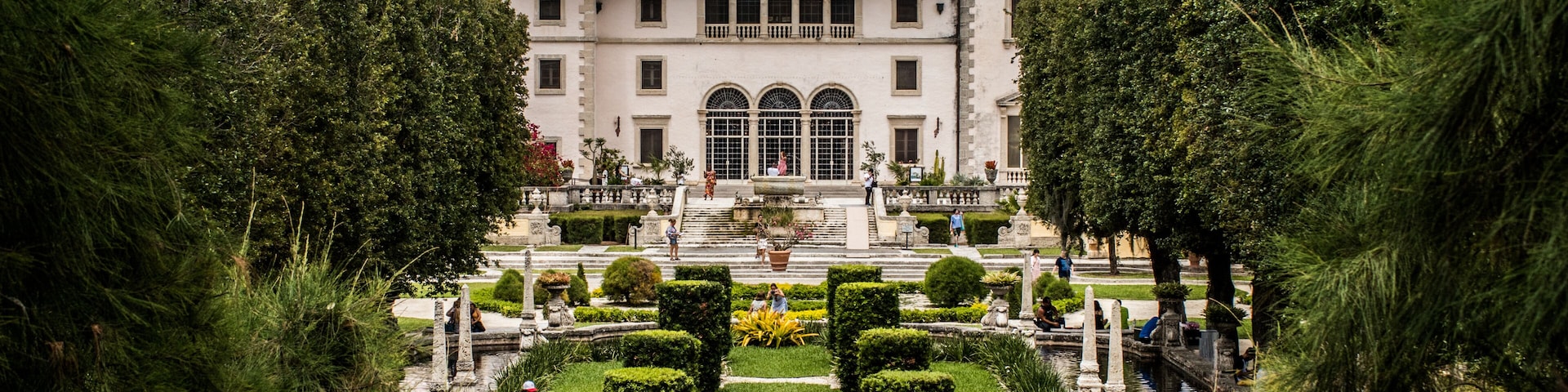 Un edificio histórico con tejado de baldosas, un patio central con fuente y un jardín circundante con setos cuidados.