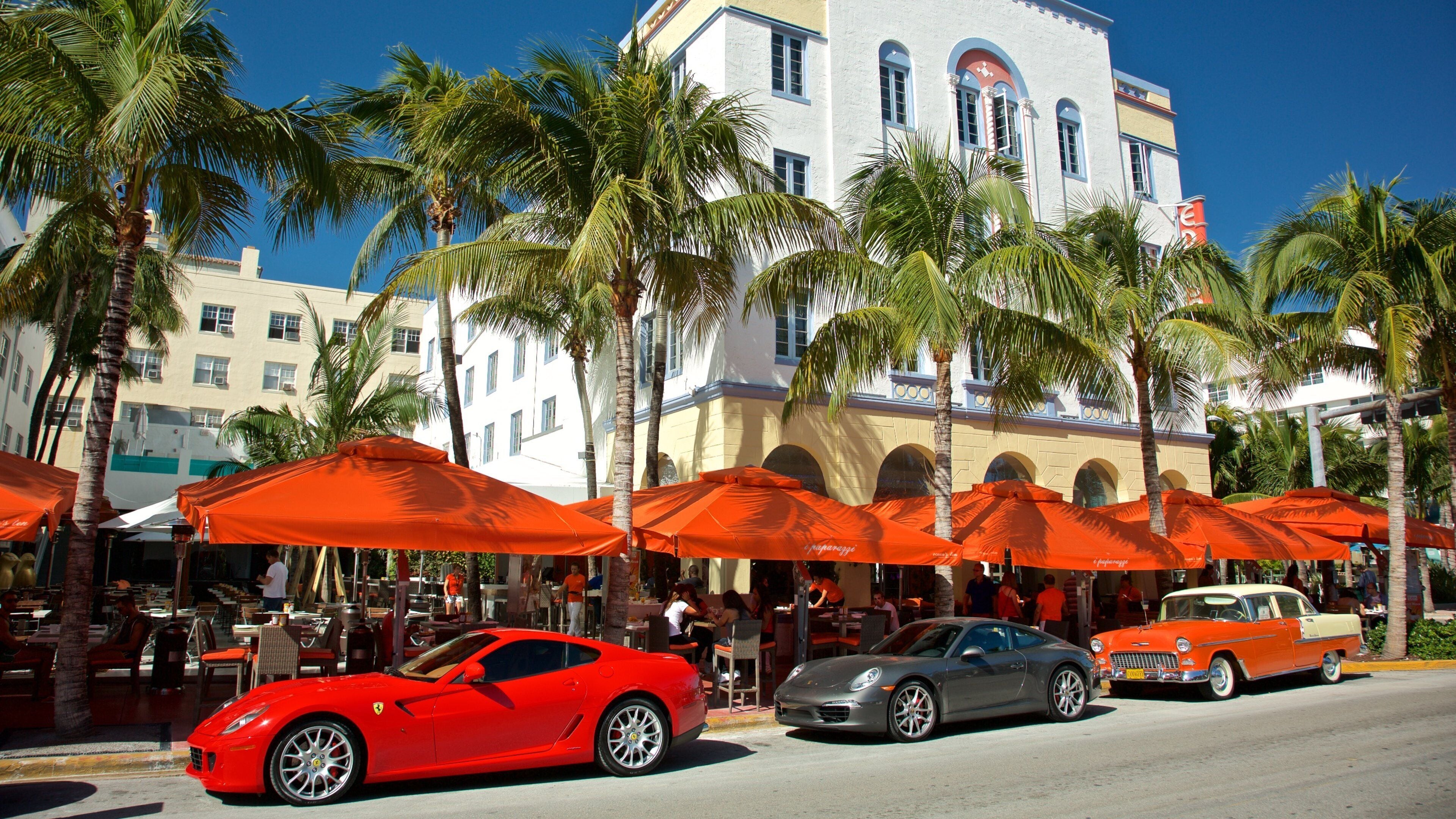 A red sports car parked on a street with palm trees and orange umbrellas in the background.