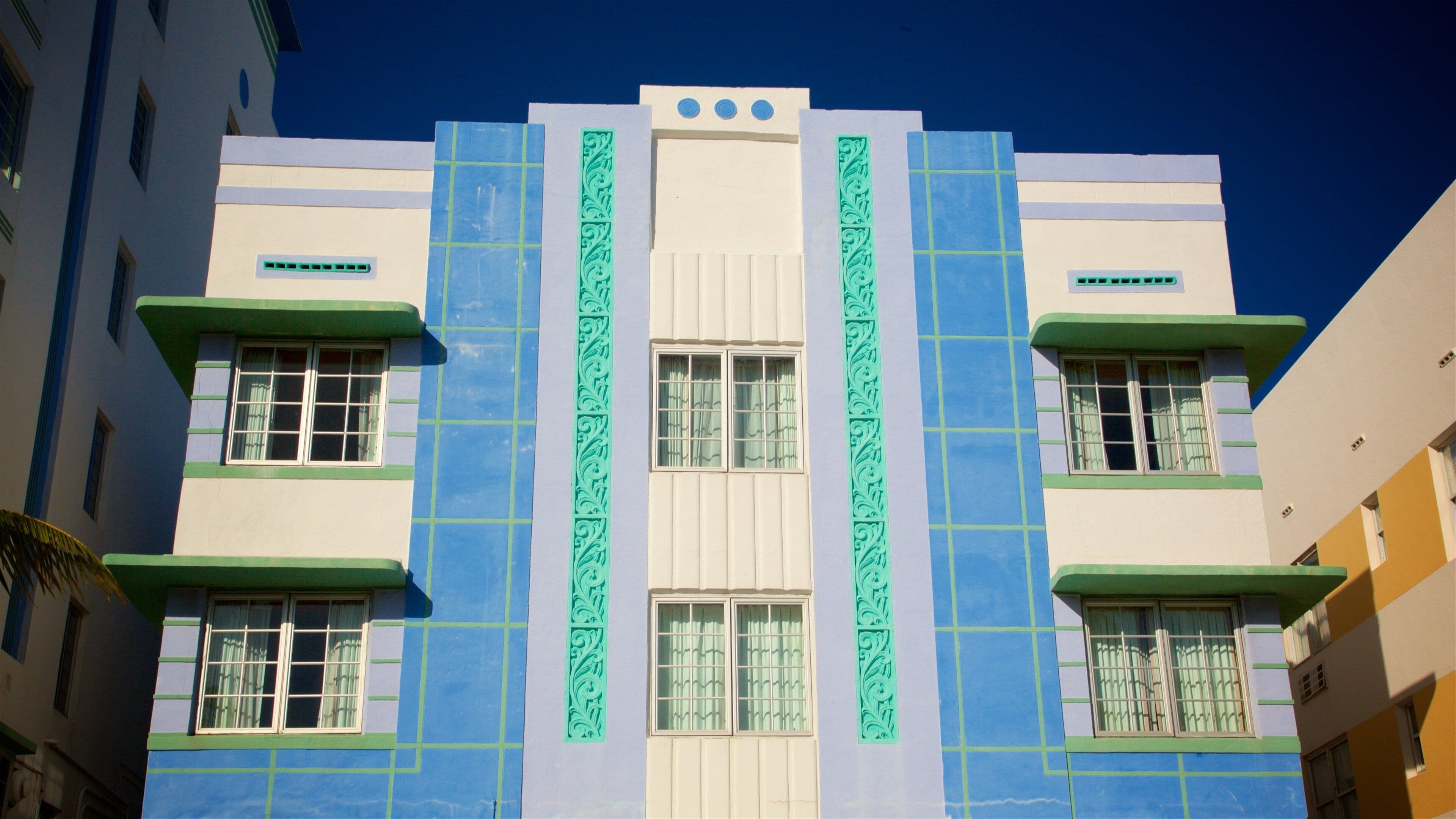 Un edificio con facciata blu e bianca, infissi verdi e decorazioni verticali.