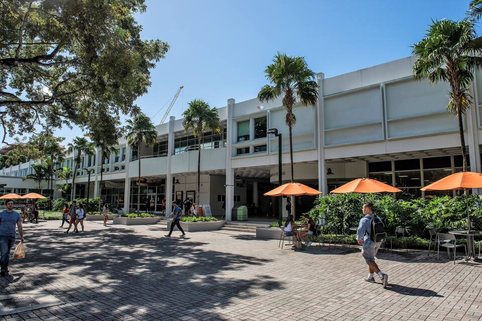 A modern building with palm trees and outdoor seating areas.