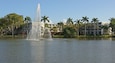 A fountain in a park with palm trees and buildings in the background.