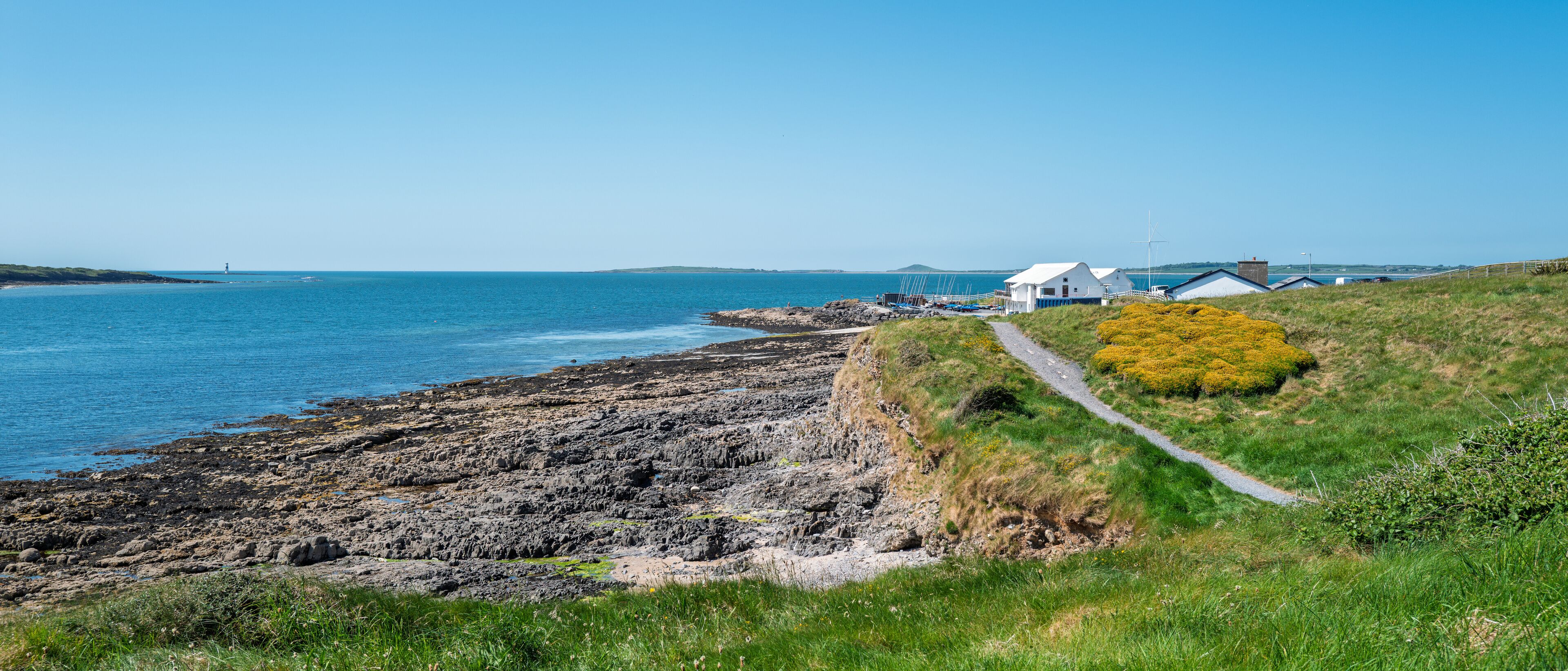 A coastal landscape with rocky shores, grassy areas, and white buildings near the water.