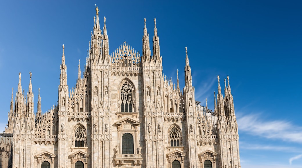 Facade of the Duomo di Milano against a clear blue sky with clouds and copy space. (Milan Cathedral 1418-1577). Church, monument symbol of Lombardy, Italy, Europe.